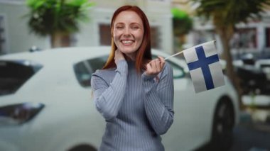 Sokakta elinde kızıl saçlı, mavi kazaklı, açık havada gülümseyen bir kadın, şehir planına karşı neşe ve gurur saçan bir kadın..