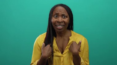 Sarı gömlekli, yeşil arka planda örgülü saçlı ve ifade edici yüzlü bir kadın..