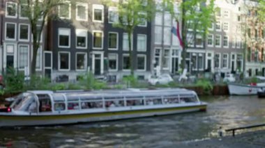 Bir tekne, ikonik binalar ve ağaçlarla dolu bulanık bir kanal manzarası. Bokeh etkisi yaratıyor. Canlı bir şehir manzarasının özünü yakalıyor..