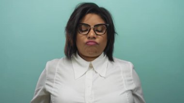 Gözlüklü ve beyaz gömlekli kadın, modern tarz ve duygulara odaklanmış saf mavi bir arkaplan karşısında düşünceli bir ifade sergiliyor..