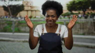 Roma harabelerinde gülümseyen önlüklü kadın, ağaçlarla ve bulanık arka plan binalarıyla dışarıdaki manzarayı kamerayla neşe içinde seyrediyor..