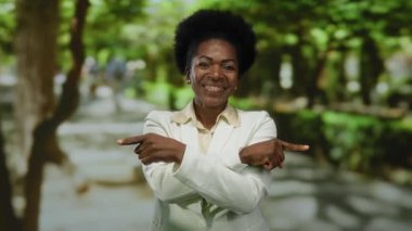 Yeşil parkı gösteren beyaz ceketli bir kadın güneşli gökyüzünün altında yön ya da seçim öneriyor..