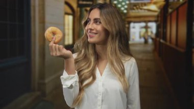 Alışveriş salonundaki dekoratif ışıkların altında gülümseyen yüzün yanında jöleli donut tutan kadın, keyif düşkünlüğü..