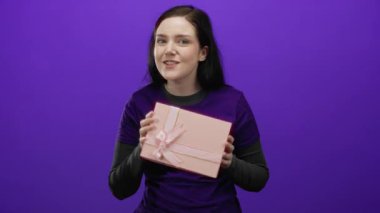 Gönüllü bir kadın, canlı mor bir arkaplan önünde gülümseyen bir hediye tutuyor. Gönüllü gömleği giyiyor. Bu, hayır kurumunu ve şenlikli atmosferde toplum ruhunu temsil ediyor..