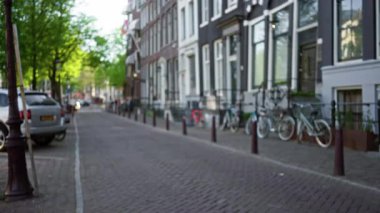 Motosiklet ve ağaçlarla kaplı zarif bir Amsterdam sokağının bulanık, bulanık manzarası, sakin bir sabah atmosferiyle Hollanda kentlerinin özünü yakalıyor..