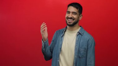 Genç adam gururla avucuna işaret ediyor canlı kırmızı bir arka plan, gösterişli bir stil ve karizma bir kot gömlek içinde dostça bir gülümseme, onun mutluluk ve cazibe vurguluyor.
