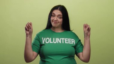 Yeşil gönüllü gömleğiyle poz veren bir kadın canlı sarı bir arka plana karşı, pozitifliği ve barış işaretleriyle güçlenmeyi ifade ediyor..