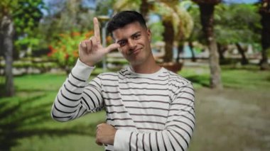 Parkta poz veren bir adam neşeli bir ifadeyle, çizgili, gür ağaçların altında.