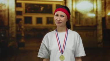 Madalyalı ve bantlı genç bir kadın kilisenin içinde derin düşüncelere dalmış bir ifadeyle, atletik başarıyı manevi ortamla harmanlıyor..