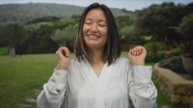 Parlak gökyüzünün altında yemyeşil ve taş yollarla çevrili sakin bir parkta neşeyle gülümseyen bir kadın..