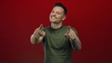 Yeşil gömlekli genç adam kırmızı arkaplanı işaret ediyor. Kendine güveni ve karizması var..