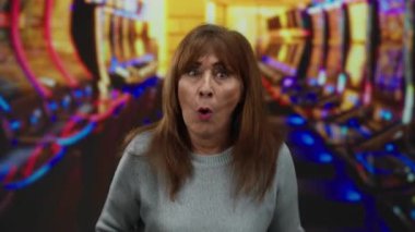 Etrafı renkli kumar makineleriyle çevrili canlı bir kumarhanede gülümseyen bir kadın neşeli oyun atmosferi sergiliyor ve İspanyol asıllıları eğlenirken yakalıyor..
