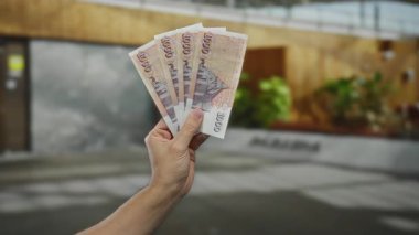 Bir şehir caddesinde İzlanda Krona banknotları tutan bir adam, bulanık arka planlı açık bir şehir ortamında para gösteriyor.