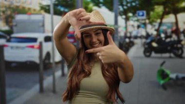Kalabalık şehir caddesinde, arka planda bulanık trafik ve yeşillik olan, şapka çerçeveli gülümseyen kadın.
