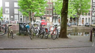 Hollanda 'nın Amsterdam kentinde çözünmüş bir kanal boyunca parkedilmiş bisiklet sürerken, Avrupa' da gün ışığında kentsel yaşamı gözler önüne seren geleneksel binalar ve yeşillikler.