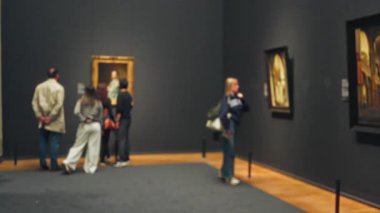 Ziyaretçiler bulanık bir müze ortamında, kapalı bir sanat galerisini keşfeden erkek ve kadınların olduğu düşünceli bir atmosfer sergileyerek sanat eserlerini seviyorlar..