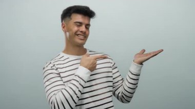 İzole edilmiş beyaz arka planda gülümserken çizgili gömlekli genç adam avucunu işaret ediyor.