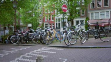 Amsterdam 'da tuğla bir sokağa park edilmiş bisikletler. Yeşil ağaçlar ve Hollanda' nın bulanık arka planında geleneksel binalar var..