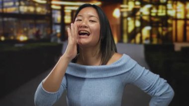 Yoğun şehir caddesinde geceleri bağıran genç bir kadın, parlayan şehir ışıklarıyla aydınlanan, açık havada enerjik bir şekilde duygularını ifade eden..