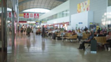 Bulanık gezginlerle dolu havaalanı terminali modern mimari ve oturma alanlarıyla dolu koridorda yürüyor..