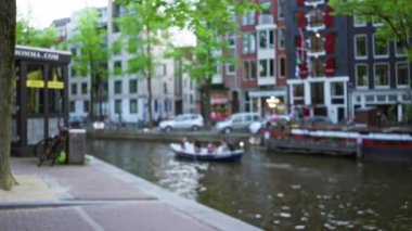 Hollanda, Amsterdam 'da bir kanal boyunca yol alan teknedeki insanların bulanık görüntüsü. Renkli evler ve yemyeşil ağaçlar..