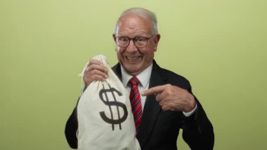 Takım elbiseli kıdemli adam dolar çantasıyla gülümsüyor, zenginliği ve yozlaşmayı simgeliyor, izole edilmiş sarı bir arka planda..