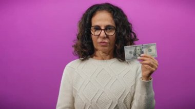 Elinde 100 dolarlık banknot tutan orta yaşlı bir kadın, göğsünde parlak bir mor arkaplan olduğunu gösteriyor. Bu da para ve kendini tanıtma arasında bir bağlantı olduğunu gösteriyor..