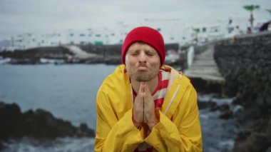 Sarı ceketli ve deniz kenarında kırmızı bereli genç adam ellerini okyanus zeminine karşı dua edercesine sımsıkı bağlamış..