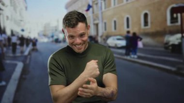 Şehir caddesinde gülümseyen genç bir adam, arka planda insanlar ve arabalar, canlı bir şehir atmosferi sergiliyor.