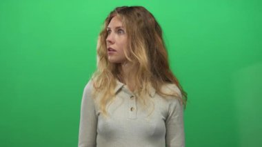 Stüdyoda ağzı açık ve şaşırmış bir kadın, yeşil ekranı geniş gözlerle gösteren sarışın bir genç deneği gösteriyor..