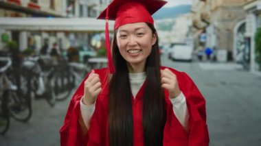 Kırmızı mezuniyet elbisesi giymiş bir kadın şehir sokaklarında gülümsüyor ve neşe ve başarı sergiliyor..