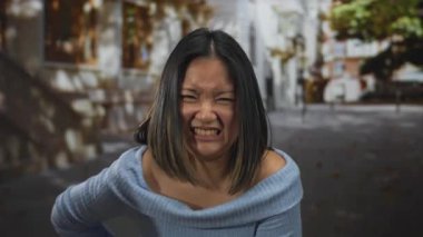 Midesi ağrıyan genç bir kadın şehir sokaklarında rahatsız bir şekilde dikiliyor, açık havada kentsel bir arka plana karşı rahatsızlık veriyor..