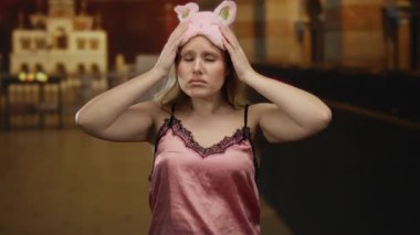 Pembe gecelikli, uyku maskeli bir kadın loş bir Katolik kilisesinde hayal kırıklığına uğramış görünüyor. Sarı saçları omuzlarının üzerinden bir anlık tefekküre dalmış.