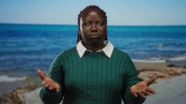 Elleriyle kendini yelleyen, deniz kenarında duran, yeşil kazak giyen, güneşli bir plaj gününde açık havada yaz esintisinin tadını çıkaran bir kadın..