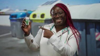 Sokakta elinde steteskopla elinde ilaç şişesi olan gülümseyen bir kadın tıbbi açıdan hayat dolu ve iyimser bir görünüm sergiliyor..