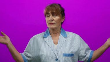 Elleri havada üniformalı bir kadın canlı pembe bir arka plana karşı duruyor, dingin ve odaklanmış görünüyor, derin düşüncelere dalmış profesyonel bir temizlikçiyi somutlaştırıyor..