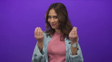 Ayrı bir mor arkaplan üzerinde el kol hareketi yapan İspanyol kadın, neşeli bir ifadeyle para aktarıyor, gündelik moda ve modern tarz sergiliyor..