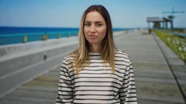 Sarışın, jestli genç bir kadın deniz kenarında gezinirken arka planda güzel mavi bir okyanus olan açık havada samimi bir anı yakalıyor.