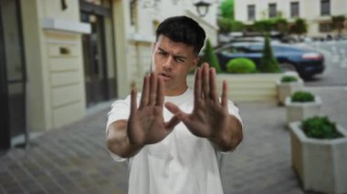 Şehir caddesinde elini kaldırmış bir adam, sanki işaret veriyormuş gibi güneşli bir günde beyaz gömlek giymeyi bırakıp dışavurumcu bir vücut dili ve ciddi bir ifade sergiliyor..