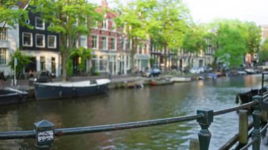 Amsterdam 'daki bulanık kanal manzarası. Klasik Hollanda evleri ve yemyeşil ağaçlarla dolu güneşli bir gökyüzünün altında yüzen tekneler..