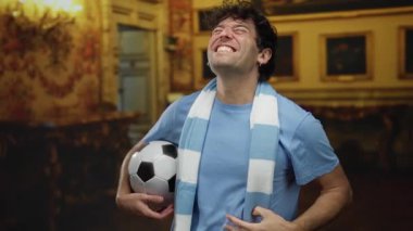 Müzede elinde futbol topu tutan mavi atkı ve neşeli ifadeli gömlek giyen İspanyol kimliğini ve kültürel ortamdaki spor aşkını sergileyen bir adam..