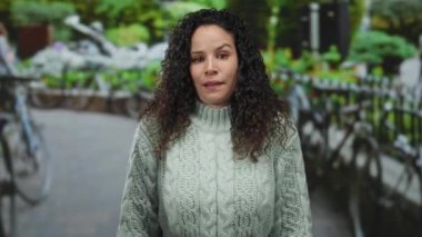 Canlı bir şehir ortamında kıvırcık saçlı kazak giyen bir kadın sokakta dikiliyor..