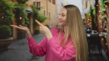 Pembe gömlekli genç bir kadın, güzel bir gökyüzü altında canlı bir açık hava yemek deneyimini somutlaştıran, restoran atmosferli büyüleyici bir terasta avucunu gösteriyor..