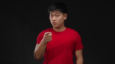 Kırmızı gömlekli genç adam siyah arka plana karşı bir telefon hareketi yapıyor, dışa kapalı ve dışa kapalı bir pozla iletişim konsepti sergiliyor..