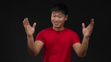 Kırmızı gömlekli genç adam, izole edilmiş siyah arkaplandan büyük jestler yapıyor. Coşku ve iletişim gösteriyor..