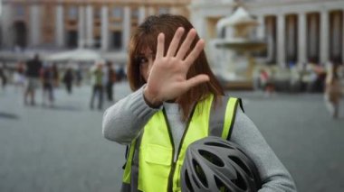 Yansıtıcı yelek giyen kadın, Vatikan 'da kalabalık bir meydanda el ele tutuşarak canlı bir şehir manzarası yakalıyor..