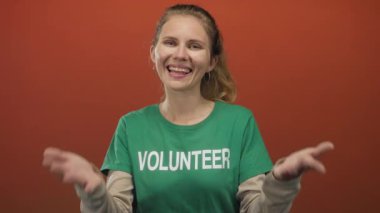 Stüdyoda gülümserken elini kaldıran genç ve yeşil sarışın tişört neşe verici bir enerji taşıyor..