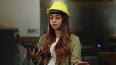 Oteldeki kadın mimar sarı kasketli, tablet kullanan kapalı bir inşaat projesinde karar verirken....