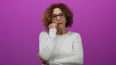 Çenesi dinlenmiş bir kadın canlı pembe bir duvarın önünde düşünceli bir ifade takınıyor.