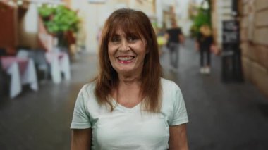 İspanyol kadın şehir arka planında bulanık bir sokakta sessiz hareketler yapıyor, canlı şehir yaşamını sergiliyor ve dinamik bir açık hava ortamında sessizliğini ifade ediyor..